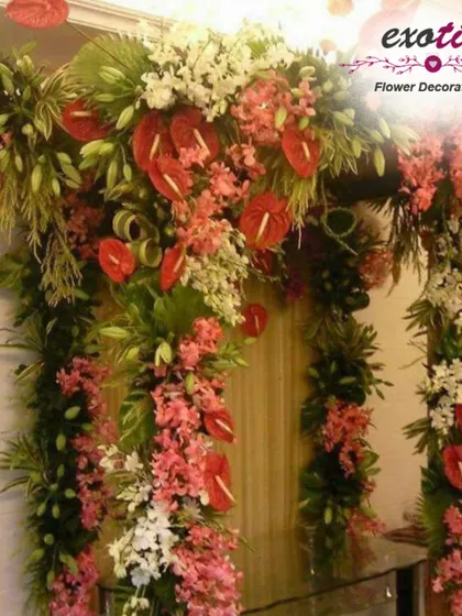 A lush and tropical floral arch. This entrance decoration is filled with red anthuriums, pink orchids, and dense greenery, ideal for a grand welcome during festive seasons.