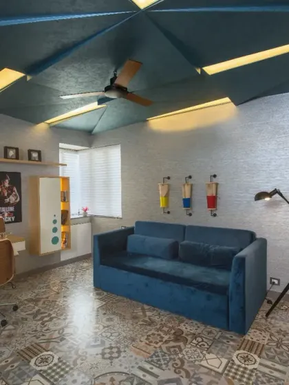 The study in the Grey Apartment is a vibrant space, featuring a geometric blue ceiling and patterned tile flooring. Quirky touches like drum-inspired wall pouches and a Rocky poster add personality and reflect the client's interests.