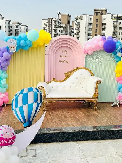 We create beautiful memories with our themed baby shower decorations, even on a rooftop. This setup includes a pastel color palette, a large crescent moon prop, hot air balloon models, and a comfortable lounge seat for the parents to be, all set against a city skyline.