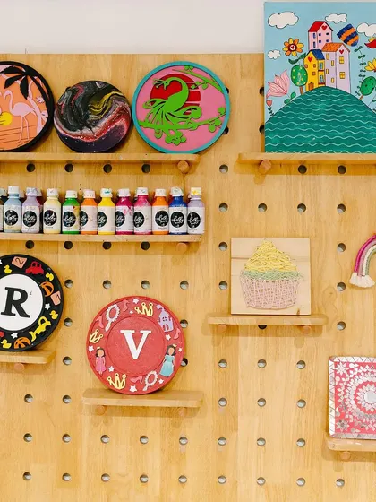 A closer look at some of the beautiful art made right here in our studio. This display features monogrammed plates, acrylic pour canvases, and other painted pieces, showing the variety of projects you can create with us.