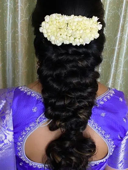 A voluminous messy braid styled with a jasmine gajra. This is a popular choice for brides who want a blend of traditional and modern hairstyling.