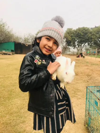 A smiling girl in a winter hat gently holding a white rabbit, clearly enjoying the experience.