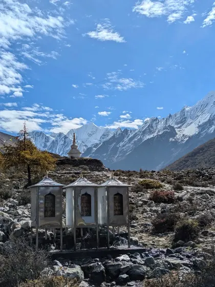 Buddhist prayer wheels and a stupa stand against the stunning backdrop of the snow-covered Langtang range in Nepal, blending spiritual heritage with natural beauty.