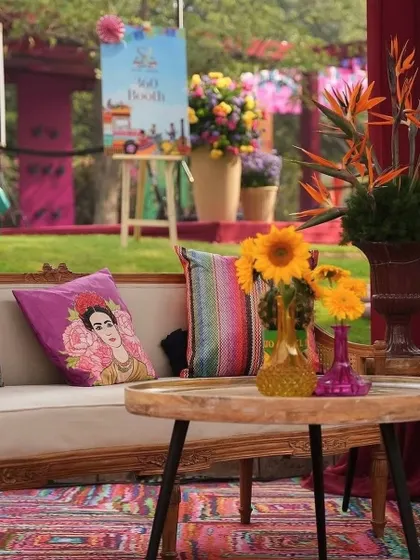 A cozy and eclectic seating area for a Mehendi, featuring a Frida Kahlo-themed cushion, colorful textiles, and bright sunflower arrangements.