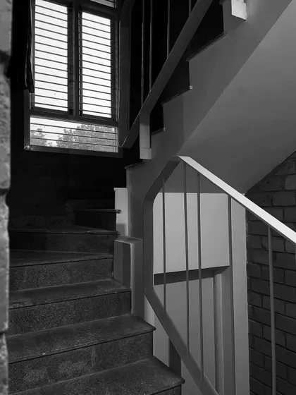 The stark contrast in this black and white shot highlights the form of the staircase and the light filtering through a louvered window.