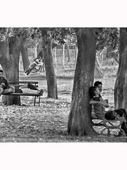 A scene from a park, capturing different couples finding moments of intimacy and rest. This black and white street photograph tells multiple small stories in a single frame, observing the quiet moments of human connection.