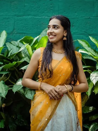 A beautiful portrait of a bride-to-be during her Haldi celebrations, looking radiant in her yellow and white outfit against a lush green background.
