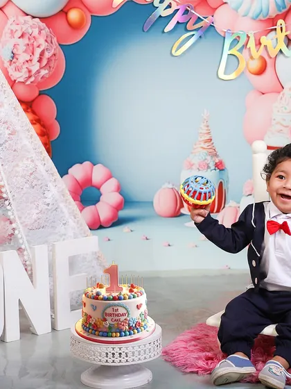 Ready to party! This dapper little one-year-old, in his suit and bow tie, is all smiles for his birthday celebration, complete with a colorful cake and festive backdrop.