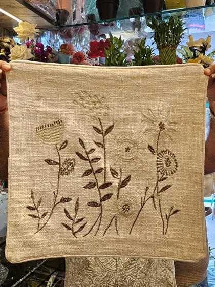 This earthy, hand-embroidered cushion cover features a delicate wildflower design. The brown thread on a natural linen base gives it a rustic, organic feel.