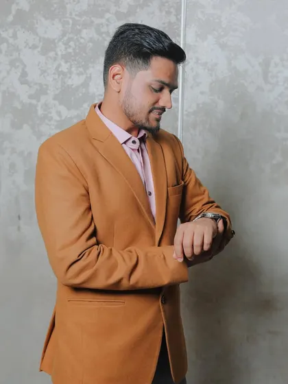 A candid shot of the groom in a stylish brown blazer, looking down at his watch as if in anticipation. This portrait has a modern and relaxed feel.