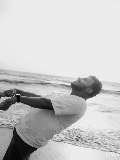 The groom's joyful expression captured in a dynamic black and white photo from a beach pre-wedding shoot.