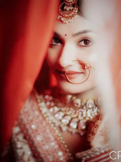 A mysterious and beautiful close-up of the bride peeking through her red dupatta, focusing on her expressive eyes.