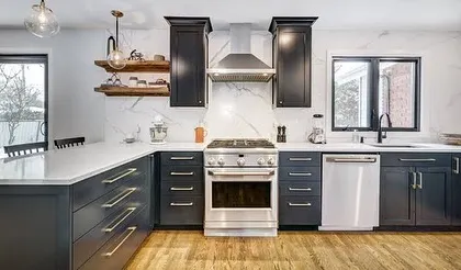 This modern kitchen design features dark blue shaker-style cabinets, a white marble-effect backsplash, and open wooden shelves. The combination of classic and contemporary elements creates a sophisticated and timeless look.