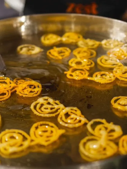 A close-up of golden jalebis frying to crispy perfection in a large kadai.