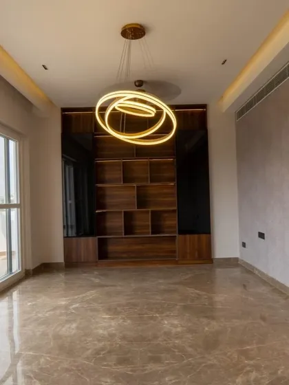 A stunning, modern chandelier acts as a piece of art in this room. The custom-built wooden shelving unit provides a beautiful backdrop, perfect for displaying books and decor.
