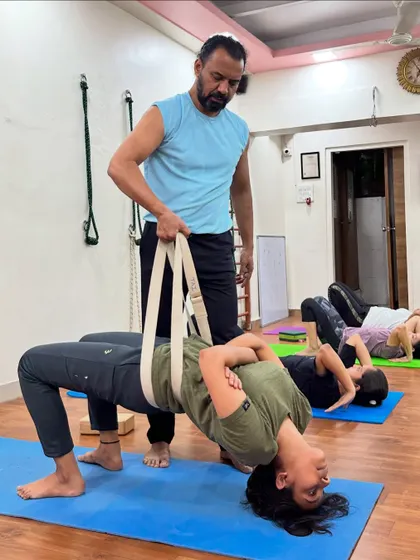 I am guiding a student through Grivasana, or the Neck Pose, using a yoga belt for support. This advanced posture is excellent for strengthening the neck and pelvic floor muscles and can also help in managing thyroid-related issues.