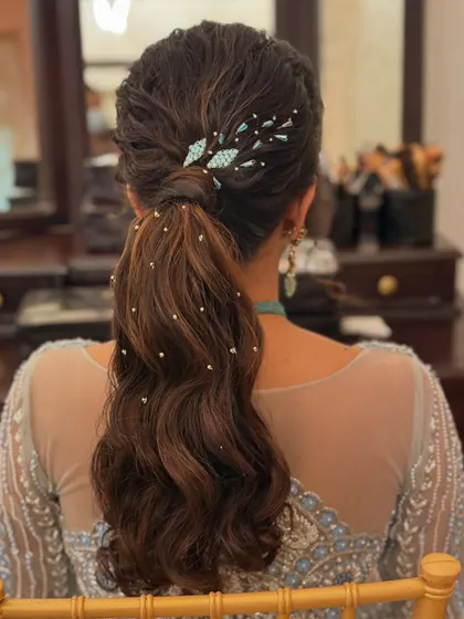 A chic and textured ponytail with soft waves. The look is elevated with a stylish blue accessory and scattered pearls for a touch of glamour.