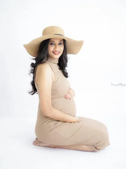 A chic and simple portrait. The mom-to-be wears a stylish beige dress and a sun hat, creating a modern and sophisticated look.