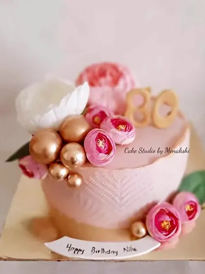 An elegant no-fondant cake for an 80th birthday. The soft pink textured buttercream is adorned with flowers and gold spheres, creating a sophisticated and celebratory design.