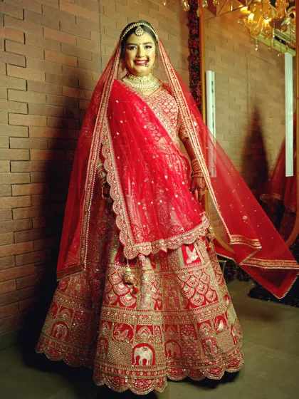 A full-length bridal portrait showcasing the magnificent red and gold lehenga. The bride's happy and confident smile makes this a perfect memory of her wedding day look.