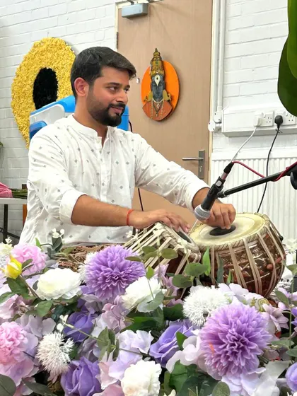 Playing at the devotional concert in the UK, surrounded by flowers and the serene presence of the deities.
