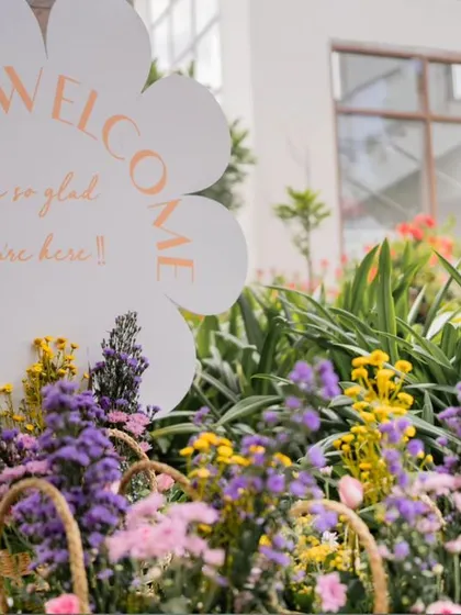 A flower-shaped welcome sign surrounded by beautiful purple and yellow flowers.