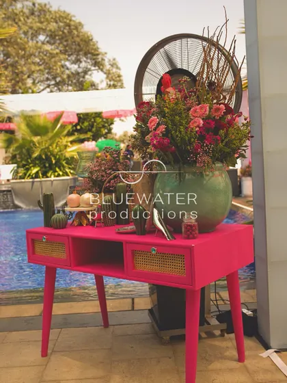 A pink console table by the pool is styled with a large floral arrangement and other decorative props.