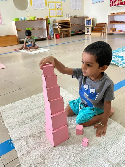 A child works with the Pink Tower, a classic sensorial material. This activity helps them visually discriminate between sizes and builds their understanding of dimensions, which is an indirect preparation for mathematics.