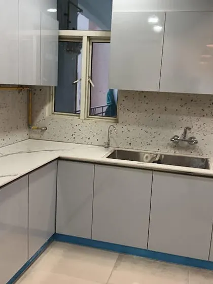 A work-in-progress shot of a modern kitchen installation. This design features light grey glossy cabinets and a white countertop with a terrazzo-style backsplash.