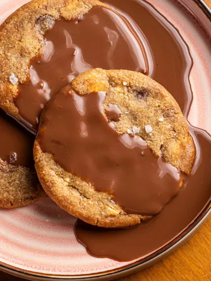 Cookies being drenched in melted chocolate at Bastian. The focus is on the glossy, smooth chocolate, creating a visually satisfying and decadent image.