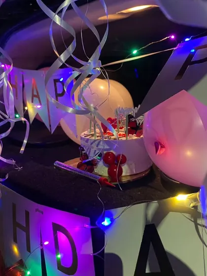 A close-up of a car boot surprise decoration. You can see the birthday cake, "Happy Birthday" banner, and colorful fairy lights, all packed into a small space for a big surprise.