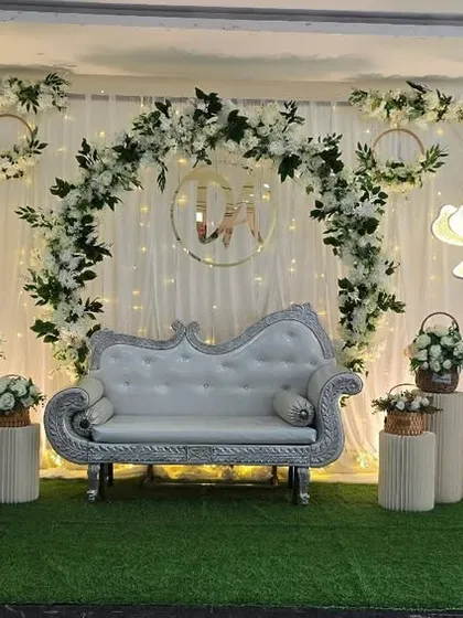 A classic wedding reception stage with a white floral arch, a custom monogram, and a silver diwan, creating a timeless and romantic setting.