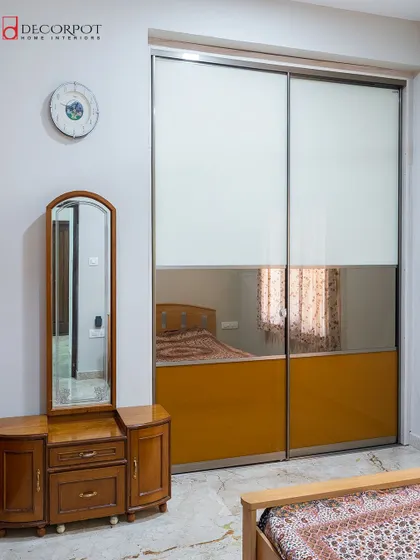 A practical and stylish sliding wardrobe with a two-tone finish. The bottom half features a reflective orange panel, while the top is a clean white, paired with a classic wooden dressing table.