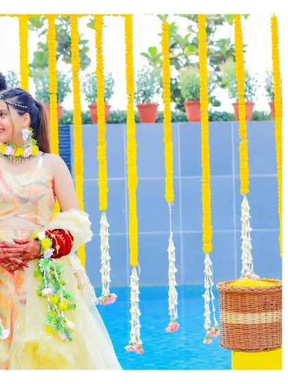 A candid portrait of the bride at her Haldi ceremony, with the vibrant yellow floral decorations creating a beautiful, bright backdrop.