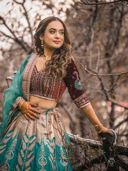 A three-quarter portrait of the woman in her stunning lehenga, posing gracefully amidst the bare branches of trees in autumn.