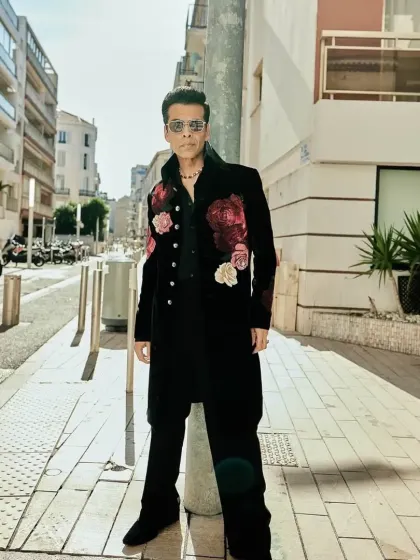 Karan Johar wearing a custom black longline jacket with bold, hand-embroidered floral motifs in shades of red and pink. This Indowestern piece is crafted from rich velvet for a truly luxurious feel.