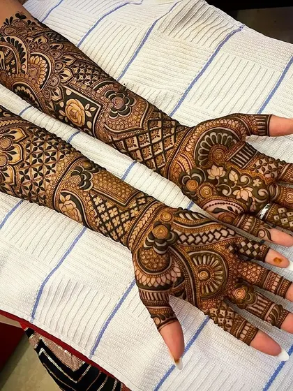This design showcases a beautiful blend of different textures, from the fine-line jaal net on the fingers to the bold, shaded floral patterns on the arms.