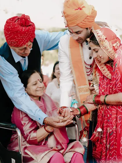 A bride and groom share a moment with an elder family member in a wheelchair during their wedding ceremony. This image is a testament to family bonds and the inclusion of all loved ones in the celebration.