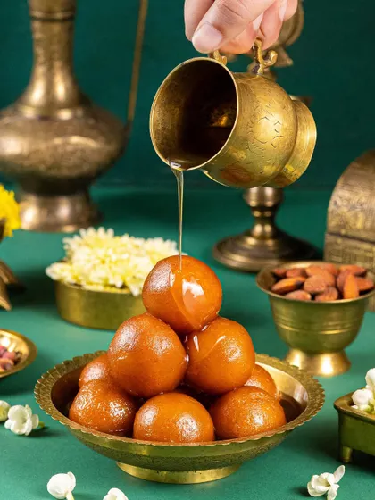 A dramatic action shot of syrup being poured over a pyramid of Gulab Jamuns, capturing the moment of indulgence.