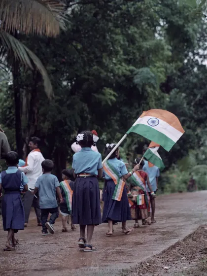 The same group of children seen from behind as they walk down a wet village road. This perspective feels more candid and observational, focusing on their collective journey.
