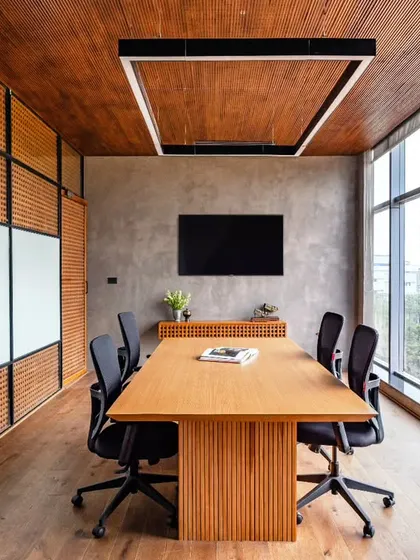 A discussion room at Anthea Pharma designed for quick meetings, featuring a striking teakwood blockwork pattern and integrated writing boards. The ceiling has wooden acoustic panels to improve sound quality, while the exposed cement TV wall adds an industrial feel.