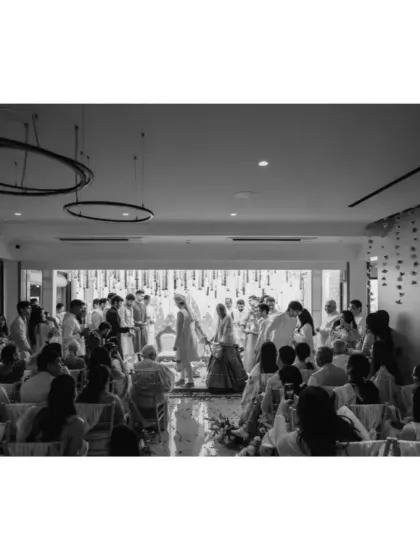 A wide black and white shot of the intimate wedding ceremony, capturing the full scene of guests witnessing the union at home.