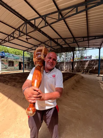 A member proudly holds a Gada in a traditional sandpit akhada. The smile on his face captures the joy and strength that comes from connecting with this ancient and powerful form of training.