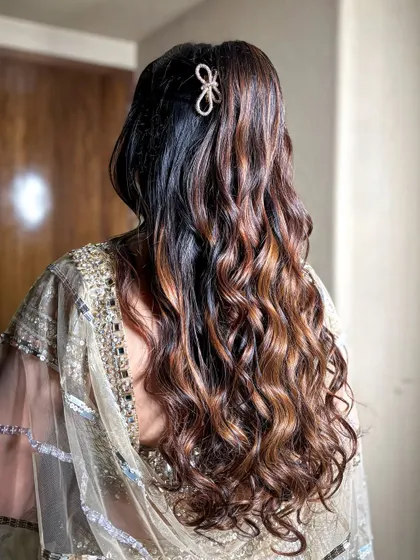 A simple yet elegant half-up hairstyle with soft curls and a delicate bow clip for a sangeet.