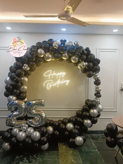 A sleek black and silver balloon ring with a neon 'Happy Birthday' sign for a 25th birthday.