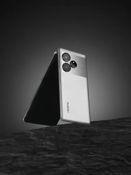 A creative shot of the realme GT6, using a piece of dark rock to create a rugged, textured foreground that contrasts with the phone's smooth design.