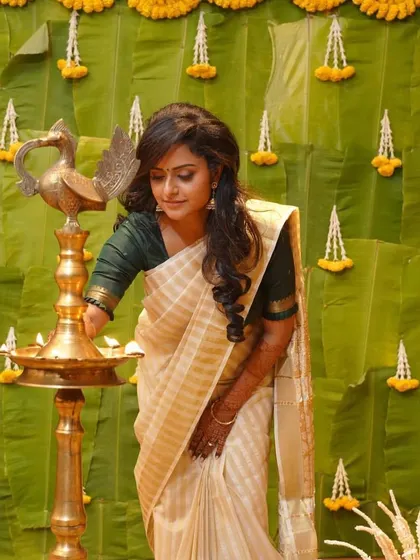 A bride in a classic Kerala kasavu saree lights a traditional lamp, against a backdrop of banana leaves.