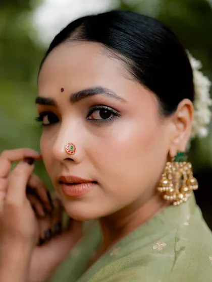 A close-up portrait of actress Anupama Gowda, focusing on her serene expression and traditional jewelry. The natural background keeps the attention on her and the details of her nose ring.