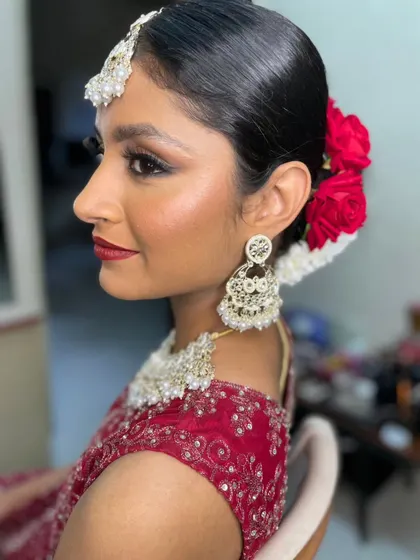 A side profile showcasing the complete bridal look. You can see the sharp winged liner, the glowing highlight on the cheekbones, and the beautiful floral bun with red roses.