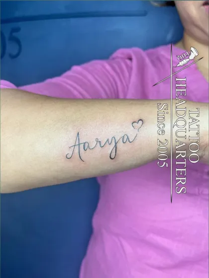 The name "Aarya" in a lovely cursive font with a heart outline at the end, inked on the forearm.